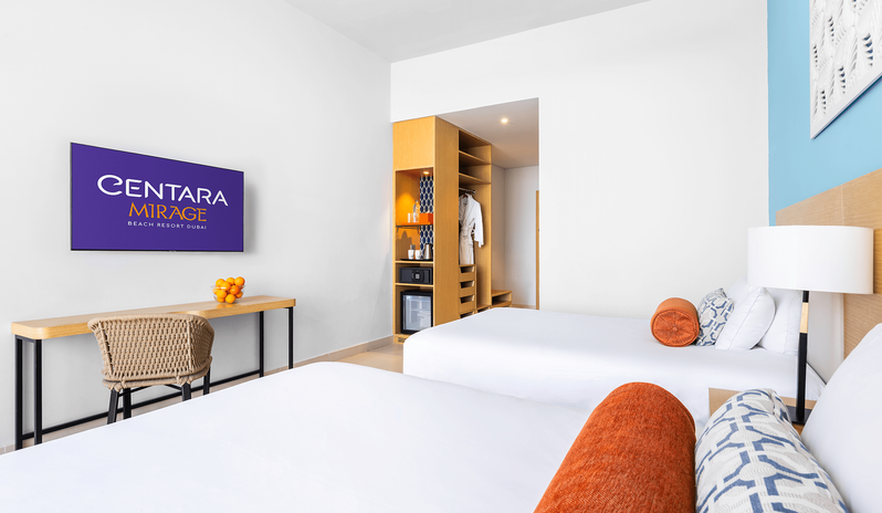 King Family Room Double Double flat-screen TV, work desk, and open closet storage next to white beds at Centara Mirage Beach Resort Dubai by Kenwood Travel