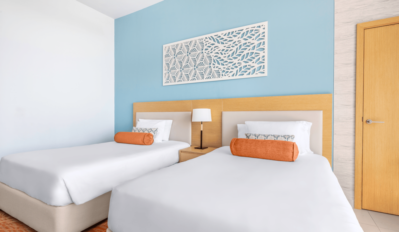 King Family Room Double Double fTwo double beds with white linens and orange bolster pillows in a family room at Centara Mirage Beach Resort Dubai by Kenwood Travel