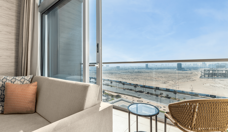 Superior Room King woven chair and small glass table, overlooking an open landscape and roads under a bright blue sky at Centara Mirage Beach Resort Dubai by Kenwood Travel