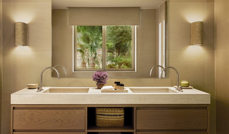 Double Room Garden View minimalist bathroom design with a floating wooden vanity, integrated stone sinks, a woven storage basket, and symmetrical warm lighting at Sani Club by Kenwood Travel