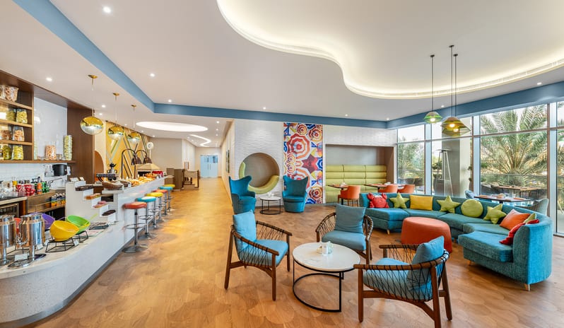 Mirage Family Lounge Large curved blue sofa with crab pillows, colorful bar stools, a snack bar, and playful geometric decor at Centara Mirage Beach Resort Dubai by Kenwood Travel