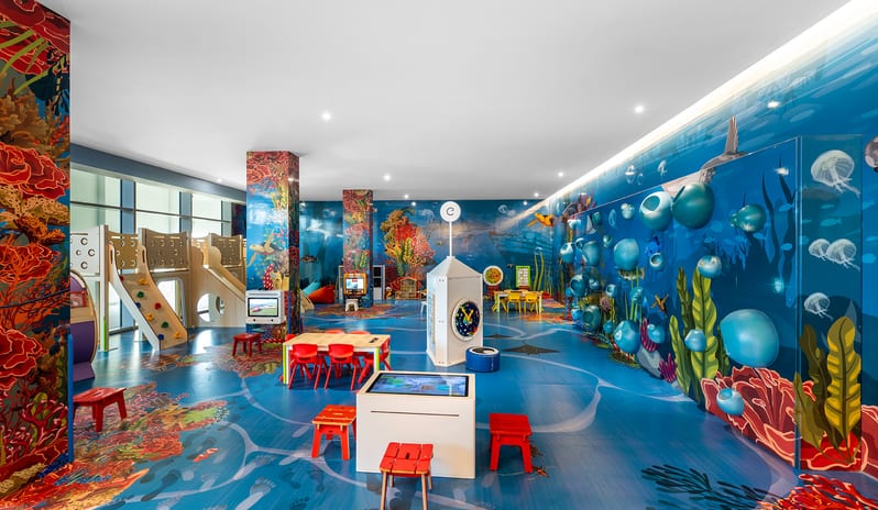 Mirage Family Lounge coral reef wall murals, a blue sea-patterned floor, climbing structures, activity tables, and small colorful stools at Centara Mirage Beach Resort Dubai by Kenwood Travel