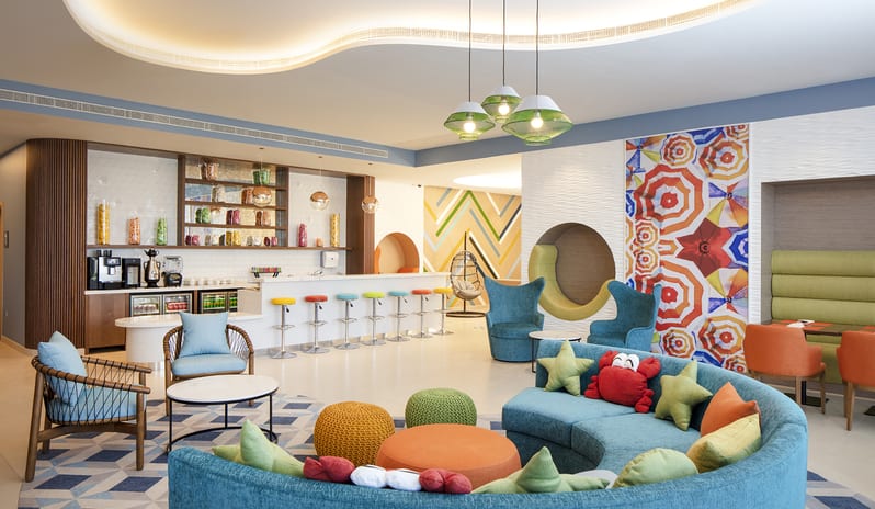 Mirage Family Lounge Large curved blue sofa with crab pillows, colorful bar stools, a snack bar, and playful geometric decor at Centara Mirage Beach Resort Dubai by Kenwood Travel
