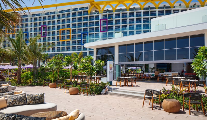 Sands Sunny outdoor lounge and patio dining area at a tropical luxury beachfront resort surrounded by palm trees and lush greenery at Centara Mirage Beach Resort Dubai by Kenwood Travel