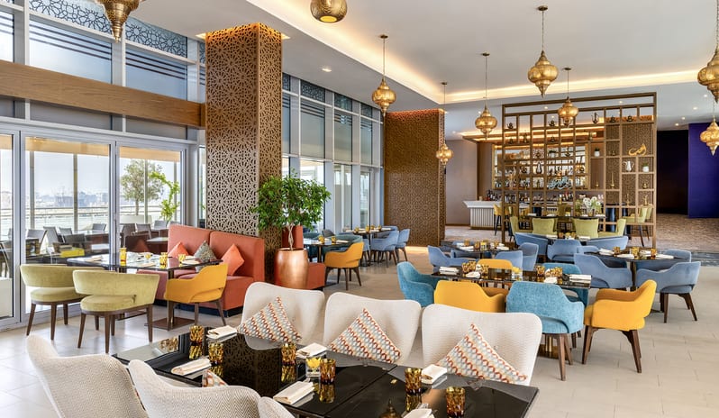 Sheesh restaurant dining area with glass tables, plush patterned cushions, and a view of an outdoor terrace at Centara Mirage Beach Resort Dubai by Kenwood Travel