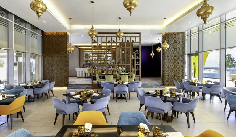 Sheesh symmetrical layout, blue and yellow armchairs, glass-top tables, and ornate Arabian pendant lighting at Centara Mirage Beach Resort Dubai by Kenwood Travel
