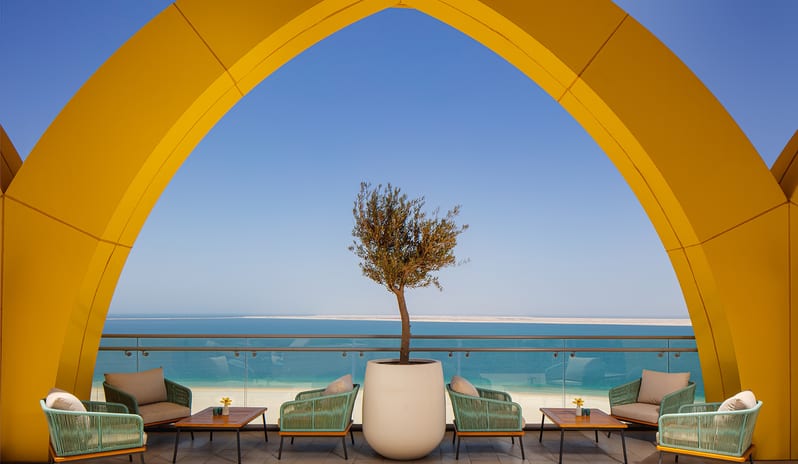 Sheesh striking yellow architectural arch framing a panoramic ocean view, sea-green lounge chairs, and a central potted olive tree at Centara Mirage Beach Resort Dubai by Kenwood Travel