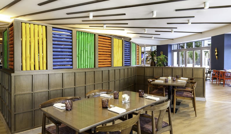 Suan Bua ontemporary restaurant dining tables set for dinner next to a bright, multicolored bamboo accent wall divider at Centara Mirage Beach Resort Dubai by Kenwood Travel