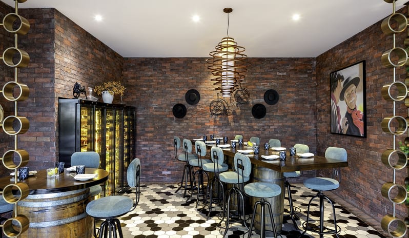 Uno Mas High-top barrel dining table with teal chairs in a brick-walled wine room at Centara Mirage Beach Resort Dubai by Kenwood Travel