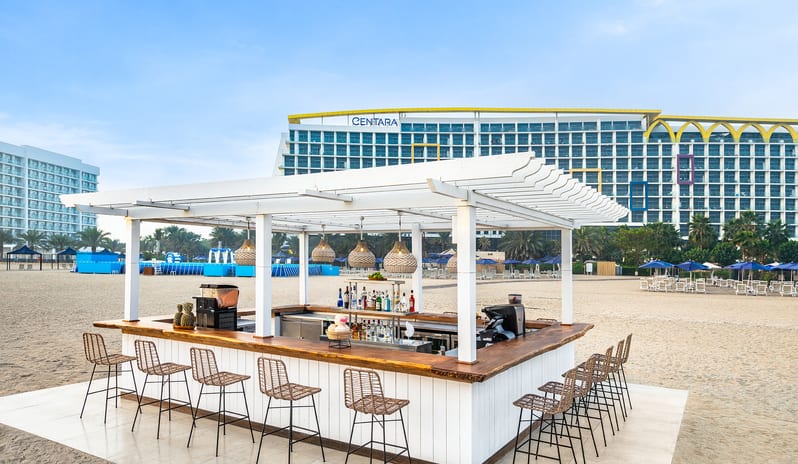 Waves Beach Bar with wicker barstools and a white pergola on the sand at Centara Mirage Beach Resort Dubai by Kenwood Travel