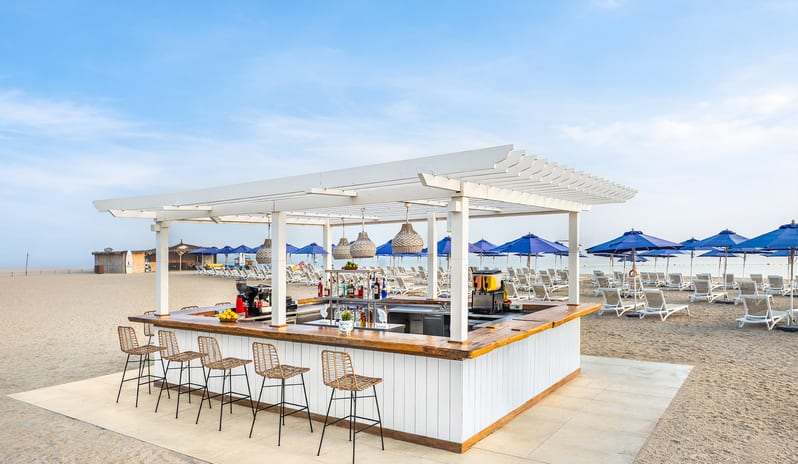 Waves Beach Bar with wicker barstools and a white pergola on the sand at Centara Mirage Beach Resort Dubai by Kenwood Travel