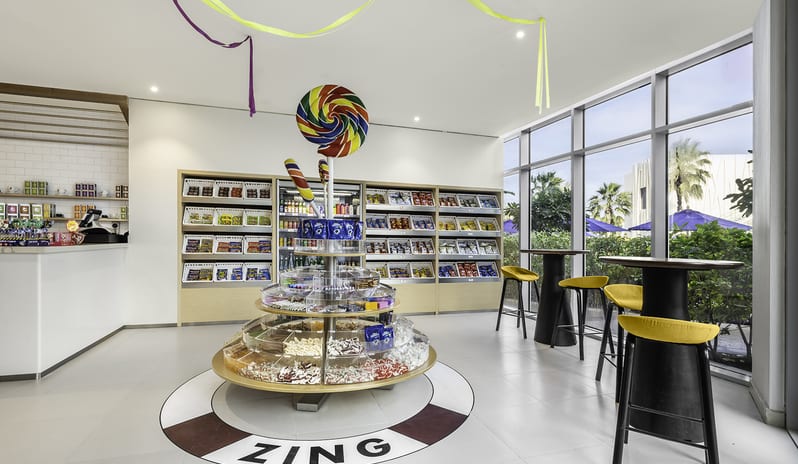 Zing central round candy fixture, packaged snack wall shelving, and tall cafe tables with yellow cushions at Centara Mirage Beach Resort Dubai by Kenwood Travel