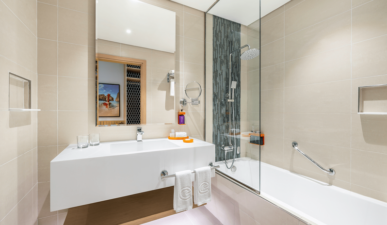 Family Room Panoramic Sea View Double Double bathroom featuring beige tiled walls, a combined bathtub and shower with a glass panel, clean white towels, and sleek fixtures at Centara Mirage Beach Resort Dubai by Kenwood Travel