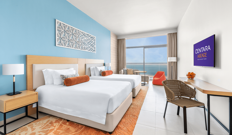Family Room Sea View Double Double Modern family hotel room with twin double beds, orange accents, and a balcony view of the sea at Centara Mirage Beach Resort Dubai by Kenwood Travel