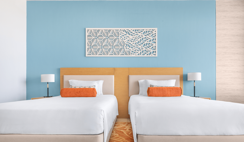 Family Room Sea View Double Double Twin double beds with bright orange pillows, a light wood headboard, and a carved white wall art panel above them at Centara Mirage Beach Resort Dubai by Kenwood Travel