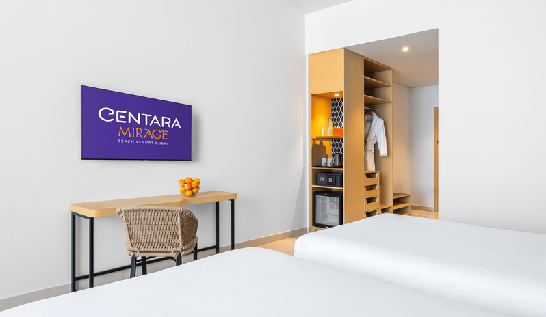 Family Room Sea View Double Double flat-screen TV, desk setup, mini fridge, and open closet storage next to two beds at Centara Mirage Beach Resort Dubai by Kenwood Travel