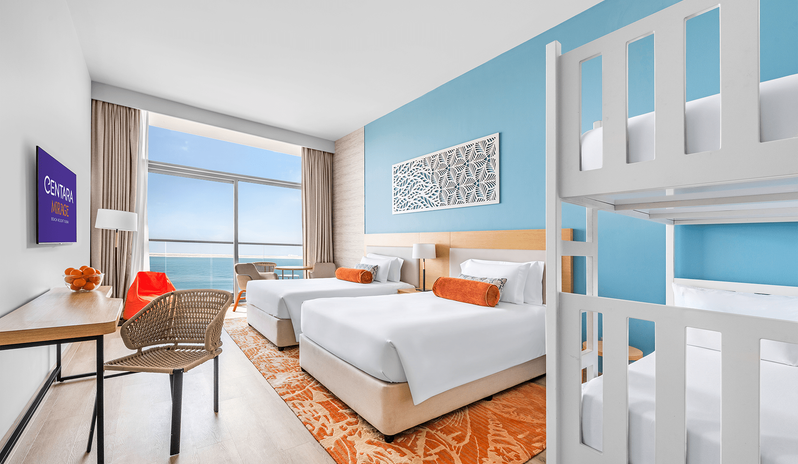Mirage Family Room Panoramic Sea View with Bunk Beds Spacious hotel room with a light blue accent wall, white bunk beds, double beds, and floor-to-ceiling windows overlooking the ocean at Centara Mirage Beach Resort Dubai by Kenwood Travel