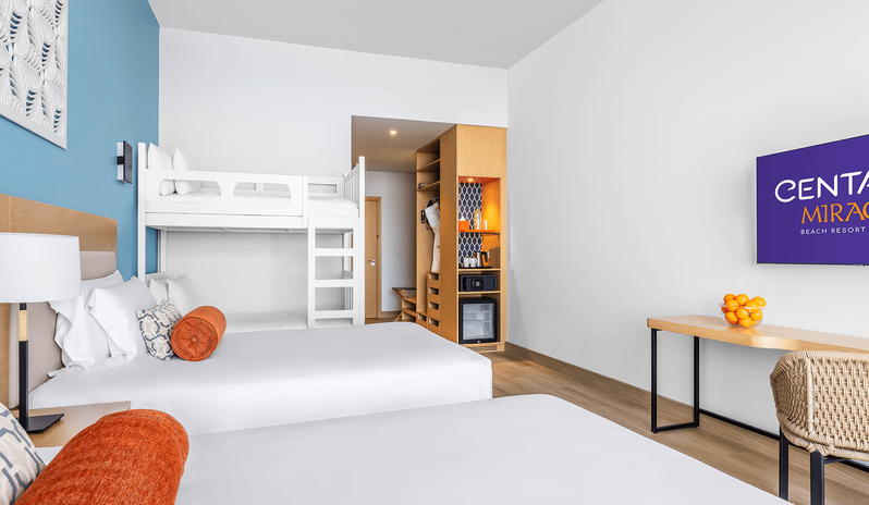 Mirage Family Room Sea View with Bunk Beds two double beds, white bunk beds, an open wooden wardrobe with a minibar and safe, and a wall-mounted TV facing a study desk with a woven chair at Centara Mirage Beach Resort Dubai by Kenwood Travel