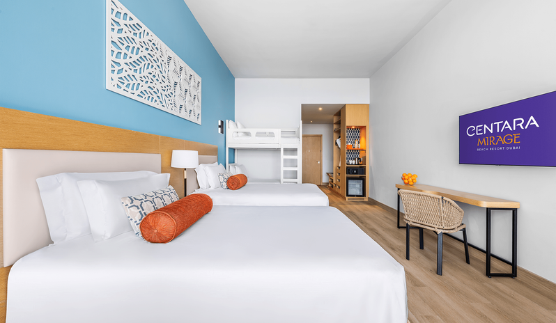 Mirage Family Room Sea View with Bunk Beds two double beds, white bunk beds, an open wooden wardrobe with a minibar and safe, and a wall-mounted TV facing a study desk with a woven chair at Centara Mirage Beach Resort Dubai by Kenwood Travel