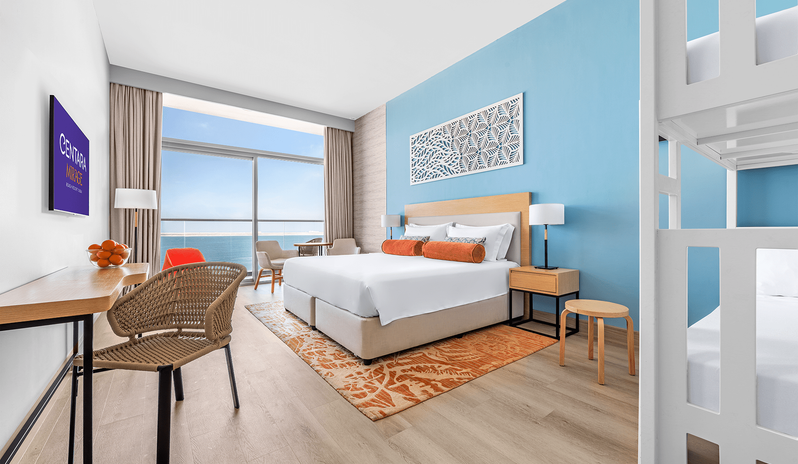 Mirage Superior Room Sea View with Bunk beds king bed, white wooden bunk beds, light blue accent wall, work desk with woven chair, and floor-to-ceiling windows overlooking the ocean balcony at Centara Mirage Beach Resort Dubai by Kenwood Travel