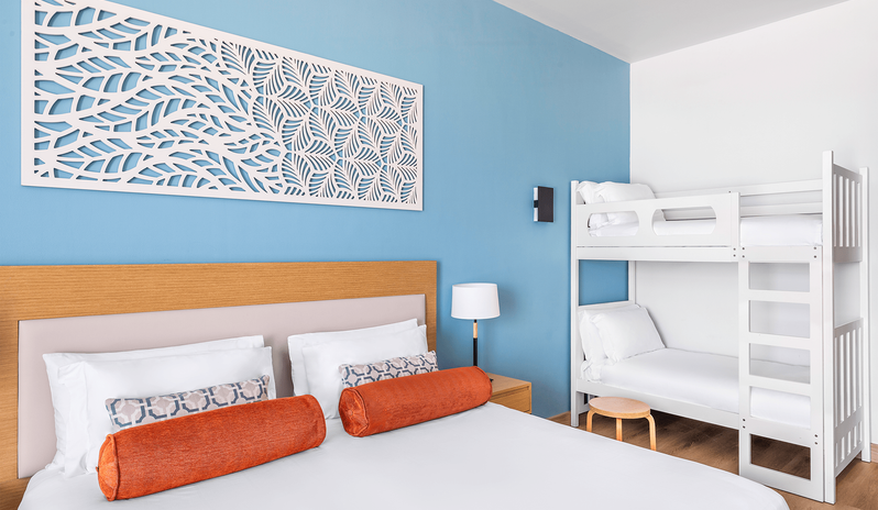 Mirage Superior Room Sea View with Bunk beds room showing a king bed with orange bolster pillows, an intricate white leaf-pattern wall art panel on a light blue accent wall, and adjacent white wooden bunk beds for children at Centara Mirage Beach Resort Dubai by Kenwood Travel