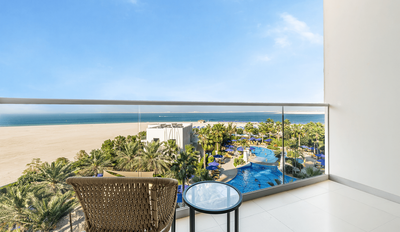 Mirage Superior Room Sea View with Bunk beds woven outdoor chair and a small glass-top table overlooking the resort's swimming pool, sandy beach, and calm blue sea at Centara Mirage Beach Resort Dubai by Kenwood Travel