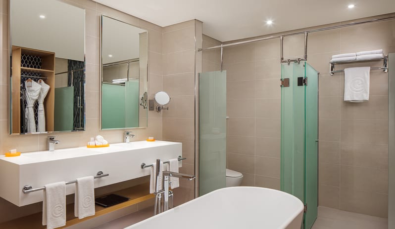 Luxury hotel ensuite bathroom featuring a contemporary double sink vanity, large mirrors, a freestanding bathtub, and a glass-enclosed walk-in shower at Centara Mirage Beach Resort Dubai by Kenwood Travel