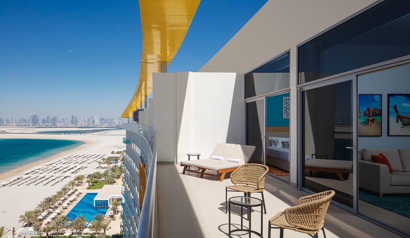 Luxury beachfront resort balcony with modern outdoor furniture, offering a panoramic view of the beach, swimming pool, and city skyline at Centara Mirage Beach Resort Dubai by Kenwood Travel