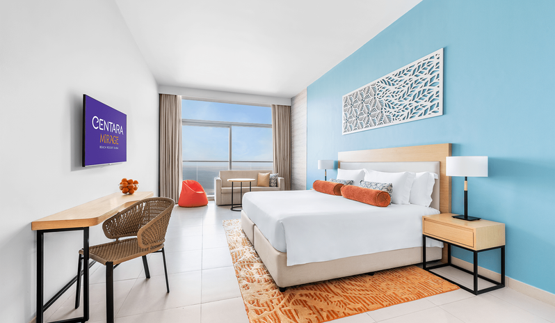 Superior Room Panoramic Sea View King Luxury hotel room with king bed, ocean view window, orange accent rug, and a wall-mounted TV at Centara Mirage Beach Resort Dubai by Kenwood Travel