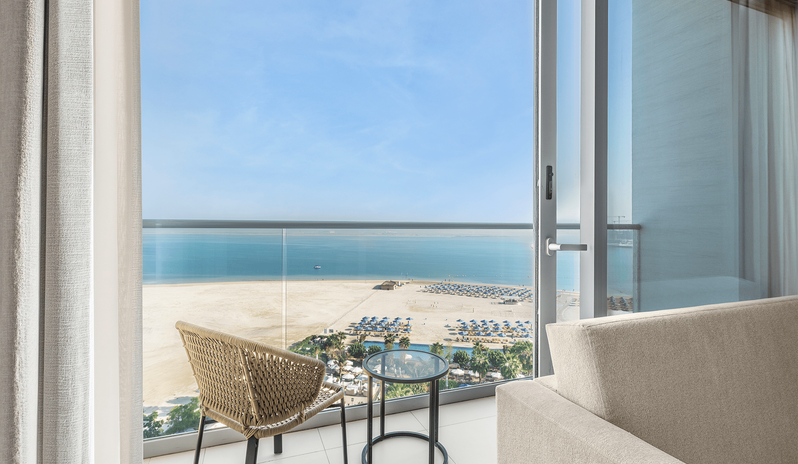 Superior Room Panoramic Sea View King Hotel room balcony overlooking a luxury beachfront resort with sun loungers, umbrellas, clear blue sea, and a bright sky at Centara Mirage Beach Resort Dubai by Kenwood Travel
