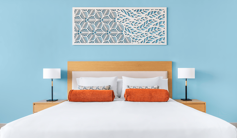 Superior Room Sea View King hotel bed with neat white bedding, orange decorative pillows, two bedside tables with lamps, and a decorative white cutout artwork hanging above the headboard at Centara Mirage Beach Resort Dubai by Kenwood Travel