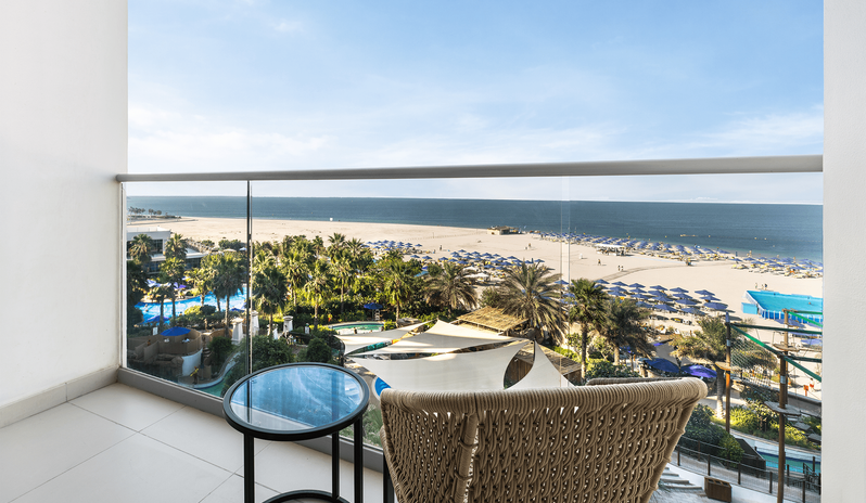 Superior Room Sea View King Private balcony with a glass railing, woven chair, and small table offering panoramic sea and beach resort views at Centara Mirage Beach Resort Dubai by Kenwood Travel