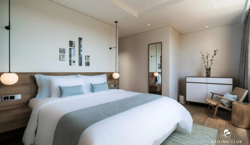 One Bedroom Pool Villa king-size bed with white and blue bedding, minimalist wooden furniture, and a woven accent chair at Sailing Club Signature Resort Phu Quoc Hotel by Kenwood Travel