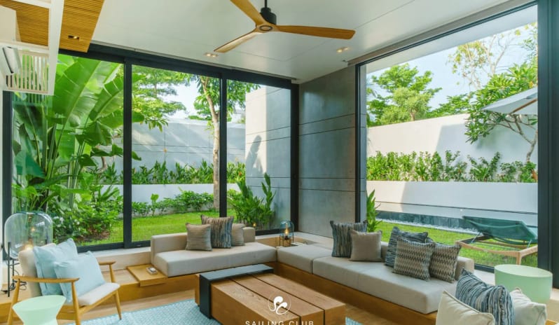 One Bedroom Pool Villa indoor lounge with minimalist furniture, a stylish wooden ceiling fan, and panoramic views of a lush outdoor courtyard at Sailing Club Signature Resort Phu Quoc Hotel by Kenwood Travel