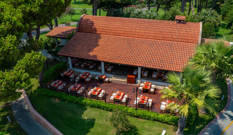 Bazilika A La Carte Restaurant featuring a terracotta tile roof and outdoor dining deck surrounded by greenery at Gloria Verde by Kenwood Travel