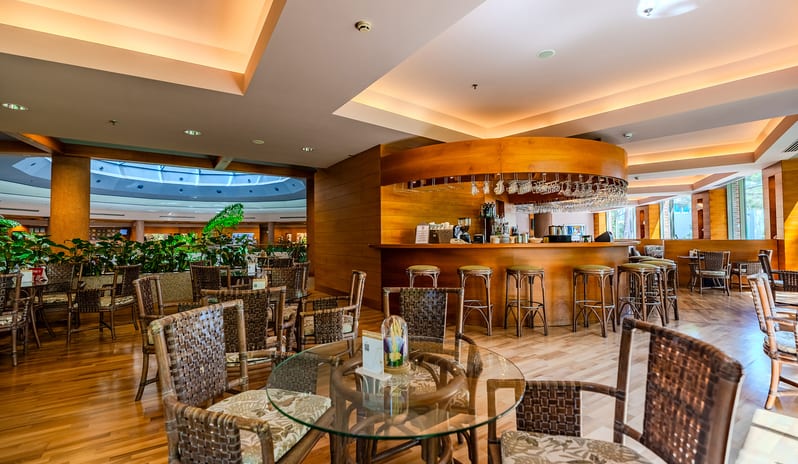 Lobby Bar woven wicker chairs, glass-top tables, and a wooden bar in the background at Gloria Verde by Kenwood Travel