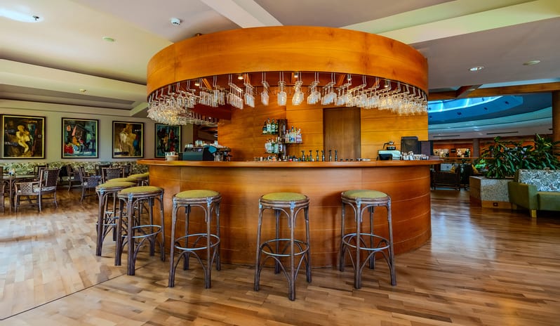 Lobby Bar polished wood paneling, elegant bar stools, and a warm seating area with paintings at Gloria Verde by Kenwood Travel