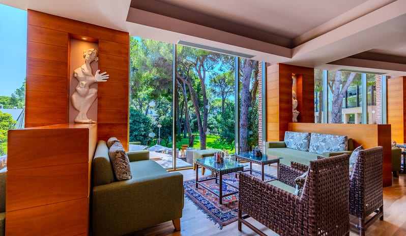 Lobby Bar green sofas, woven armchairs, and floor-to-ceiling windows with garden views at Gloria Verde by Kenwood Travel