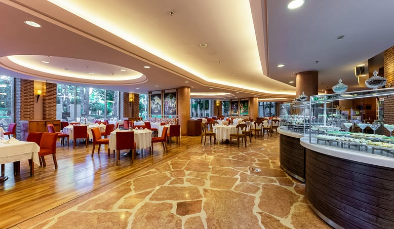 Mythos Elegant resort dining hall with stone flooring, curved lighting, and buffet stations at Gloria Verde by Kenwood Travel
