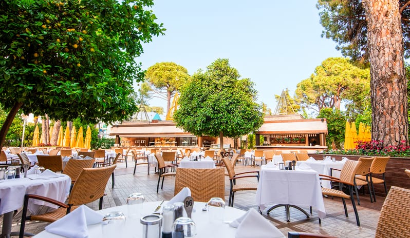 Mythos Al fresco resort dining patio with elegant table setups under lush green trees and citrus plants at Gloria Verde by Kenwood Travel