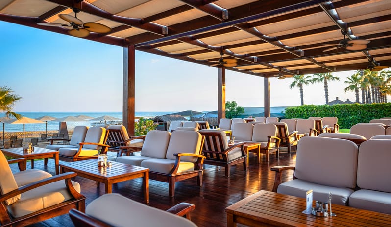 Neptuno Bar comfortable outdoor sofas, wooden tables, ceiling fans, and a scenic sea horizon at Gloria Verde by Kenwood Travel