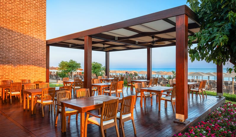 Neptuno Bar beach bar patio with wooden furniture, ceiling fans, and a scenic view of the ocean and sun loungers at Gloria Verde by Kenwood Travel