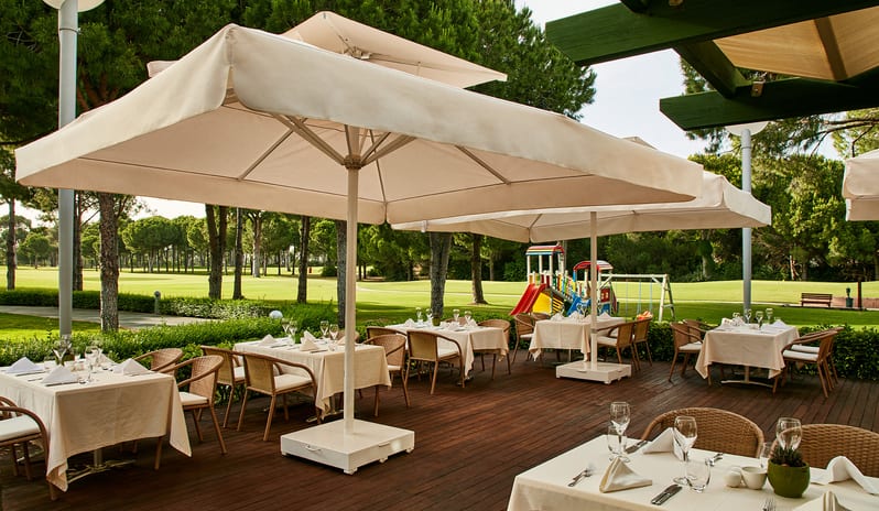 Select Restaurant Outdoor wooden dining deck at Select Restaurant in Gloria Verde Resort with large white patio umbrellas and a view of the golf course at Gloria Verde by Kenwood Travel