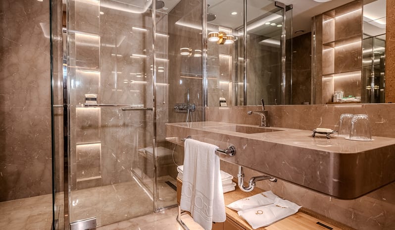 Vip Villa en-suite bathroom design with beige marble tile surfaces, contemporary chrome fixtures, plush white towels, and warm under-vanity ambient lighting at Gloria Serenity Resort by Kenwood Travel