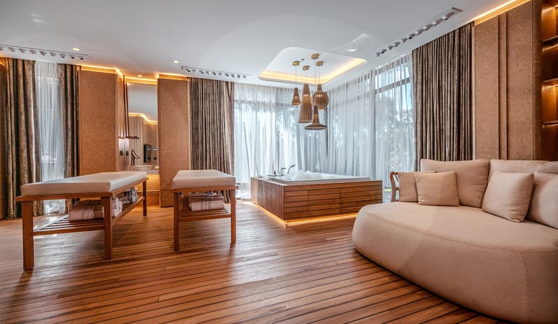 Vip Villa two massage tables, a large wood-paneled jacuzzi, a curved lounge sofa, and warm ambient lighting over wooden floors at Gloria Serenity Resort by Kenwood Travel