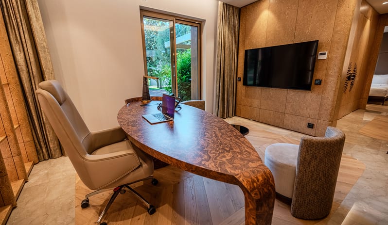Vip Villa two featuring an organic-shaped wood burl executive desk with a laptop, a leather desk chair, a wall-mounted TV, and an accent wall with a wood finish at Gloria Serenity Resort by Kenwood Travel