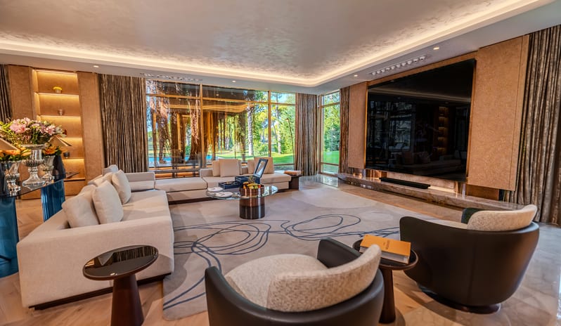 Vip Villa open-plan villa sitting room with a large swirl-patterned area rug, glass coffee table, polished marble and hardwood floors, tray ceiling lighting, and rich brown drapes at Gloria Serenity Resort by Kenwood Travel