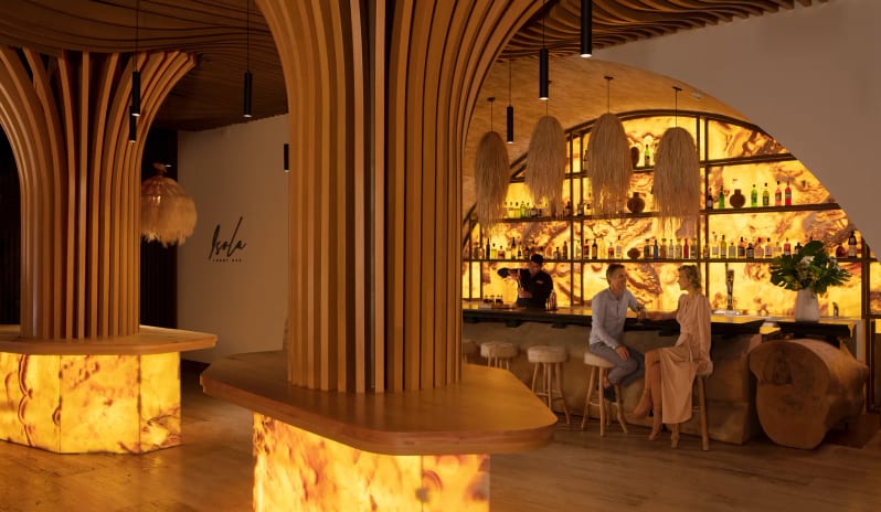 Isola lobby bar with dramatic backlit lighting, architectural wood features, and guests enjoying drinks at Impression Isla Mujeres by Secrets by Kenwood Travel