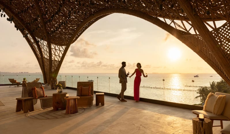The Temple Couple enjoying drinks at sunset on a luxury hotel rooftop terrace with unique architectural bamboo framing at Impression Isla Mujeres by Secrets by Kenwood Travel