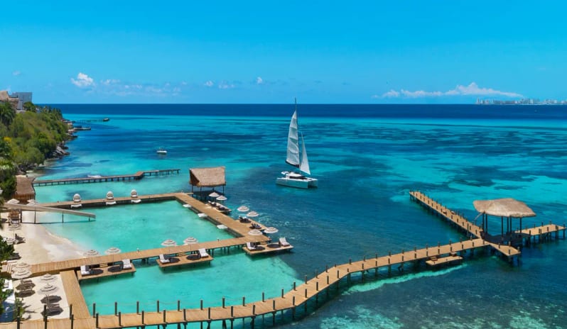 Spezia oceanfront resort with wooden piers and a sailboat anchored in turquoise sea water at Impression Isla Mujeres by Secrets by Kenwood Travel